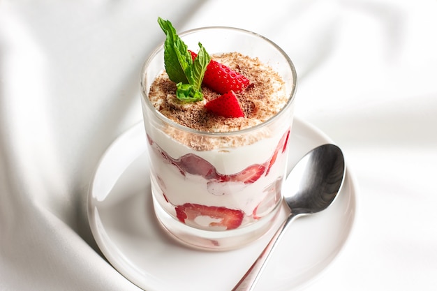 Dessert santé en verre avec fraises fraîches et yaourt à la crème sur fond blanc