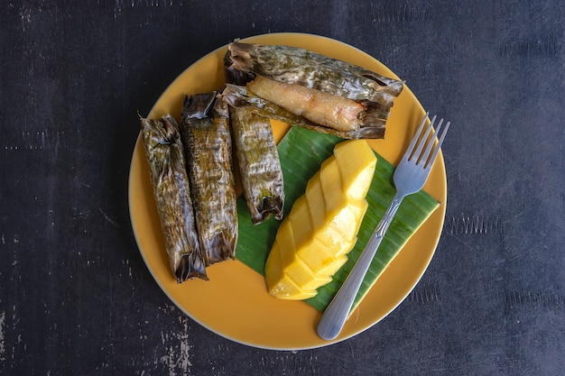 Dessert de style thaï, mangue jaune avec riz gluant à la banane dans des feuilles de palmier. La mangue jaune et le riz gluant sont des desserts traditionnels populaires de Thaïlande. Fermer
