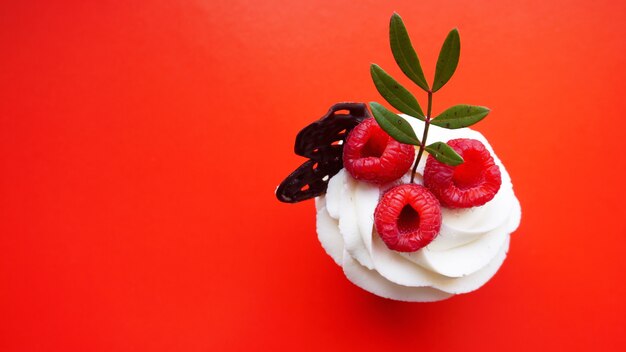 Dessert sucré fait main, cupcake avec crème au beurre et framboise sur surface rouge