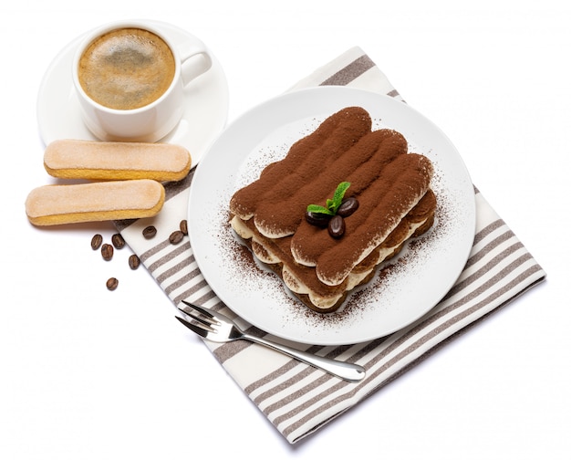 Dessert tiramisu classique sur plaque en céramique, biscuits savoiardi et tasse de café isolé sur une surface blanche avec un tracé de détourage