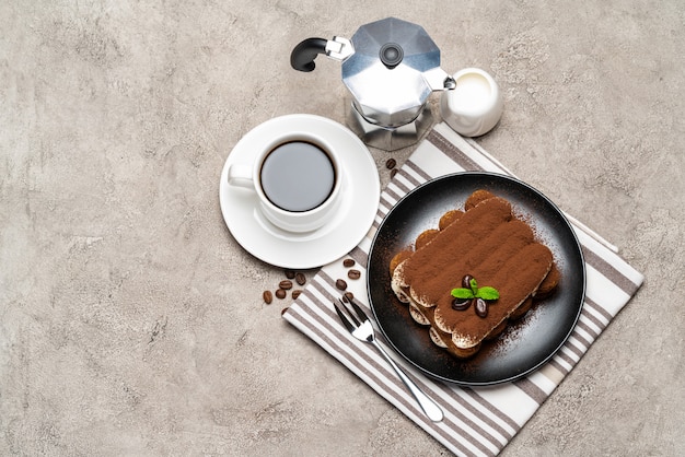 Dessert tiramisu classique sur plaque en céramique, lait ou crème et tasse de café sur une surface en béton