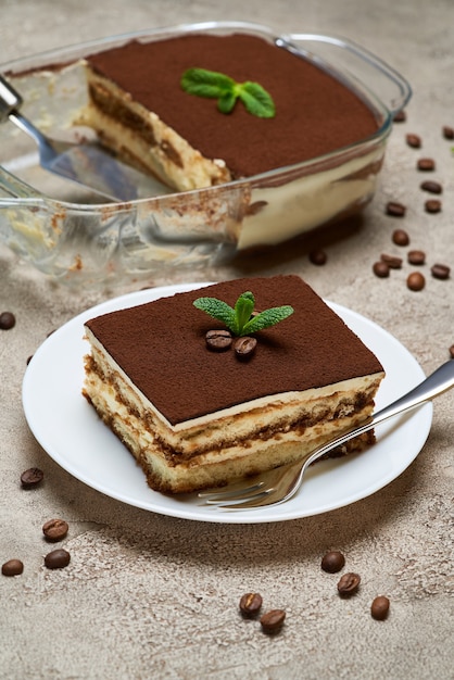 Dessert tiramisu italien traditionnel dans un plat de cuisson en verre et portion sur table en béton gris