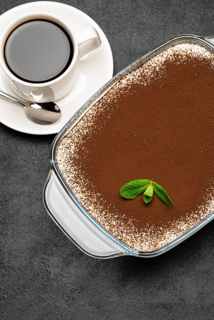 Dessert traditionnel Tiramisu italien dans un plat de cuisson en verre et tasse de café expresso chaud frais sur fond de béton ou table
