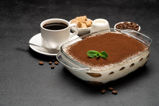 Dessert traditionnel Tiramisu italien dans un plat de cuisson en verre et tasse de café expresso chaud frais sur fond de béton ou table