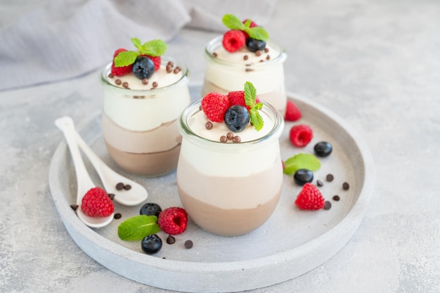 Dessert trois chocolats dans un bocal en verre avec des myrtilles fraîches, des framboises et des mûres sur le dessus