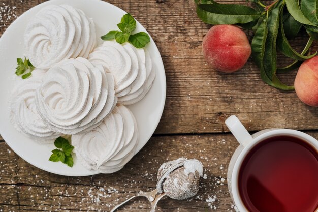 Dessert zéphyr (guimauve) sur une assiette blanche, une tasse de thé et des fruits sur la table, vue de dessus, thé de l'après-midi dans le jardin. Bonbons russes aérés, mise en page sur table vintage