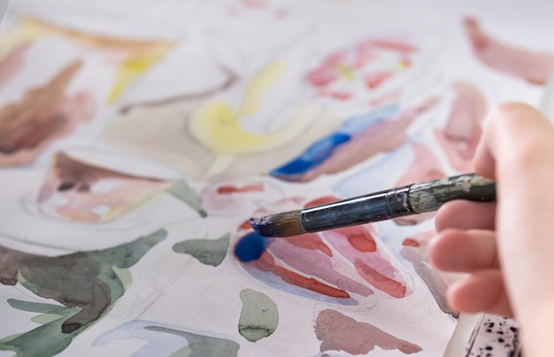 Dessin à l'aquarelle sur une feuille blanche Une jeune femme peint à l'aquarelle à la maison sur une feuille blanche