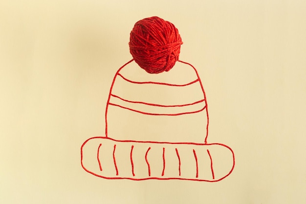 Photo dessin d'un chapeau d'hiver rouge à partir de fils de laine avec une boule intégrée à tricoter concept créatif à plat