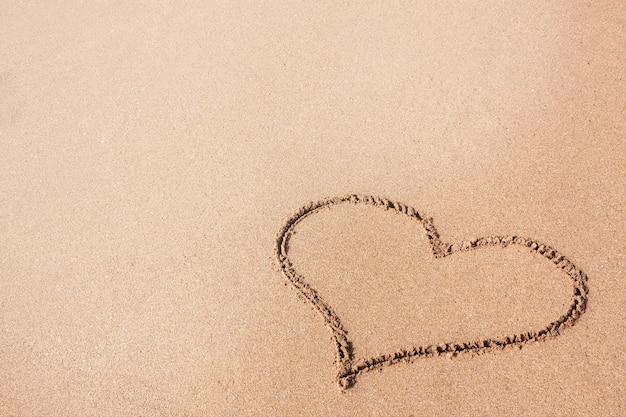 Dessin d'un coeur sur un gros plan extrême de plage de sable jaune.