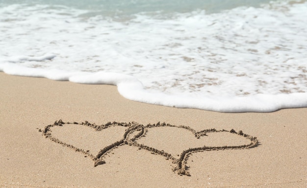 Dessin dans le sable par l'océan de deux coeurs