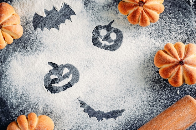 Dessin de décorations d'Halloween sur fond de farine, gâteaux en forme de citrouille et rouleau à pâtisserie. Concept de cuisine d'Halloween