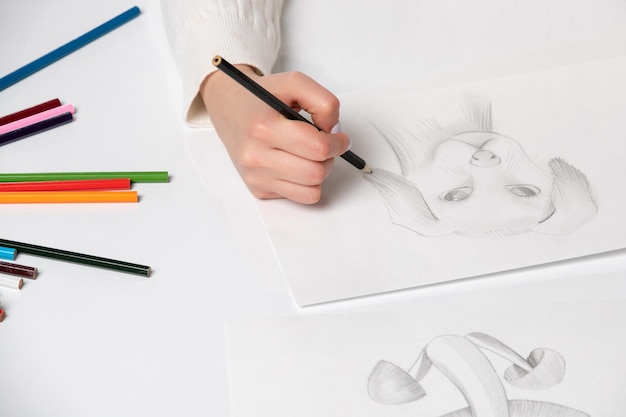 Dessin d'une main de jeune fille dessinant un chien mignon avec un crayon noir sur une table pleine de crayons colorés