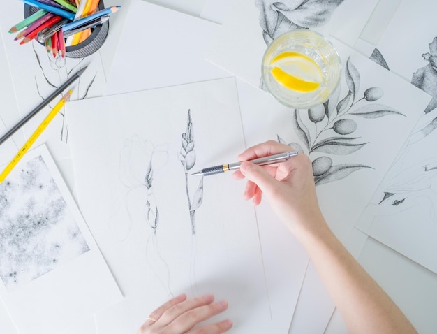 Des dessins au crayon sont sur la table Une jeune femme d'apparence européenne dessine avec un crayon sur du papier blanc Graphiques Le processus de dessin avec un crayon à la maison sur une table blanche