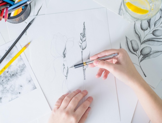 Des dessins au crayon sont sur la table Une jeune femme d'apparence européenne dessine avec un crayon sur du papier blanc Graphiques Le processus de dessin avec un crayon à la maison sur une table blanche