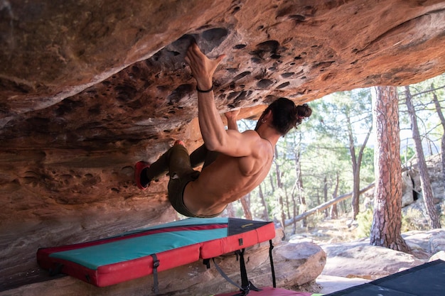 De dessous vue arrière du jeune sportif avec torse nu escaladant le toit rocheux naturel