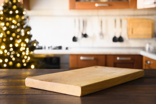 Dessus de table en bois avec planche à découper et cuisine floue avec fond de sapin de Noël pour l'affichage ou le montage de vos produits