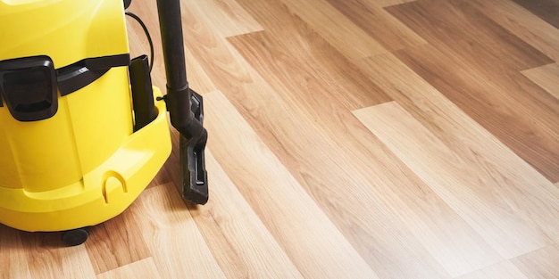 Détail de l'aspirateur jaune sur sol stratifié en bois - espace pour le texte à droite.