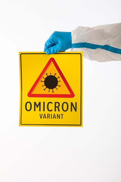 Détail d'un bras d'une infirmière médicale portant un EPI et des gants en latex avec un panneau jaune avec un symbole de danger COVID-19 qui se lit comme suit : « variante Omicron ». Concept de coronavirus, de pandémie et de santé.