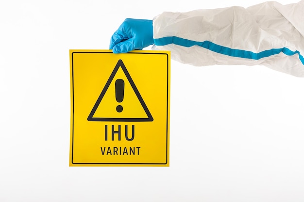 Détail d'un bras d'une infirmière portant un EPI et des gants en latex avec un panneau jaune avec un symbole de danger qui se lit comme suit : ''IHU VARIANT''. Concept de coronavirus, de pandémie et de santé.