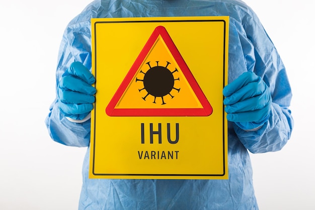 Détail d'un bras d'une infirmière portant un EPI et des gants en latex avec un panneau jaune avec un symbole de danger qui se lit comme suit : ''IHU VARIANT''. Concept de coronavirus, de pandémie et de santé.