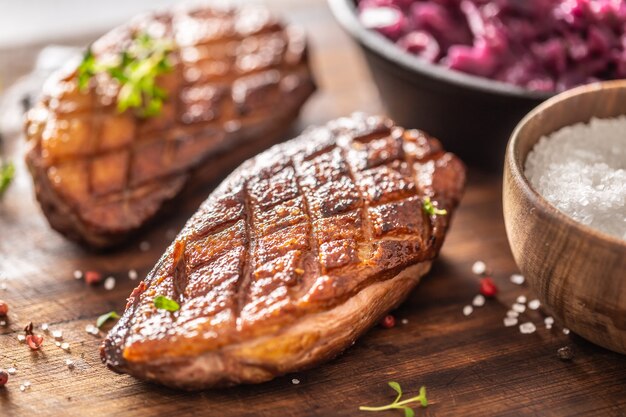 Détail de délicieux magrets de canard rôtis et compote de chou rouge sur une planche à découper en bois.