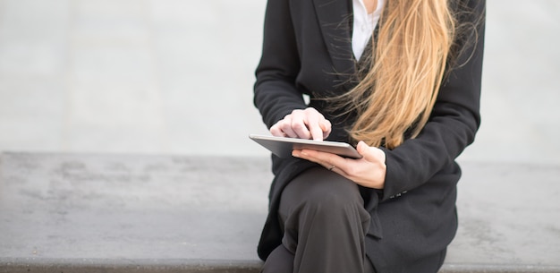 Détail d'une femme d'affaires à l'aide de sa tablette assis sur un banc dans une ville