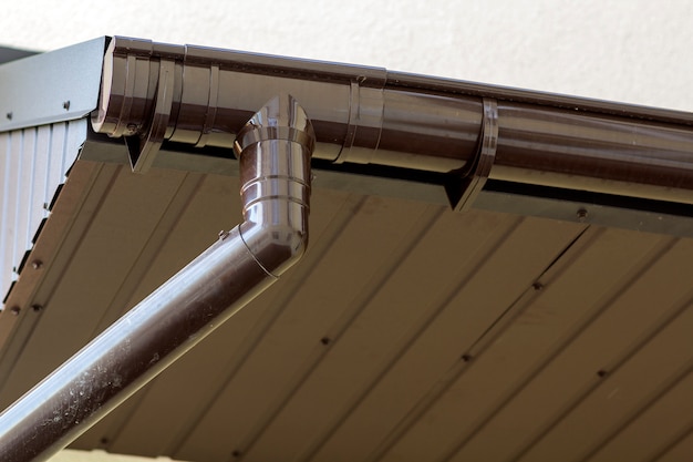 Détail en gros plan du coin de la maison de chalet avec revêtement en planches de métal brun et toit avec système de pluie de gouttière en acier. Toiture, construction, installation de tuyaux de drainage et concept de raccordement.