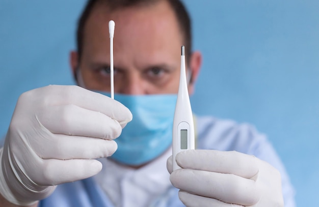 Photo détail de l'infirmière montrant dans ses mains un thermomètre et un coton-tige pour recueillir des échantillons organiques