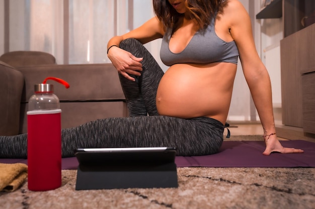 Détail d'une jeune femme caucasienne enceinte avec un t-shirt gris effectuant des exercices de pilates Exercices en ligne dans les cours de pré-partum bien-être pendant la grossesse