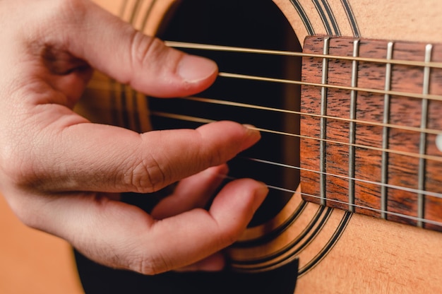 Détail main masculine jouant des cordes de guitare acoustique