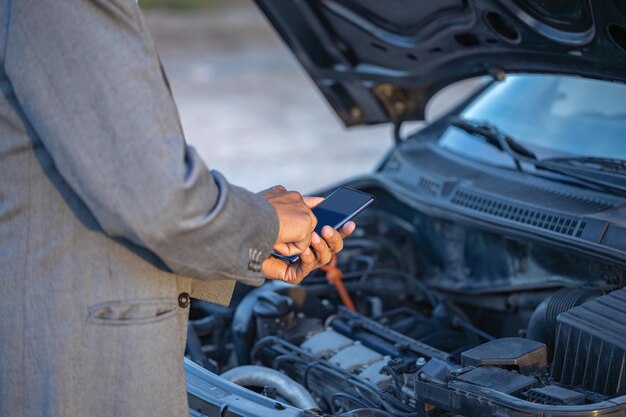 Détail des mains d'un homme latino avec son téléphone portable avec sa voiture en panne en arrière-plan