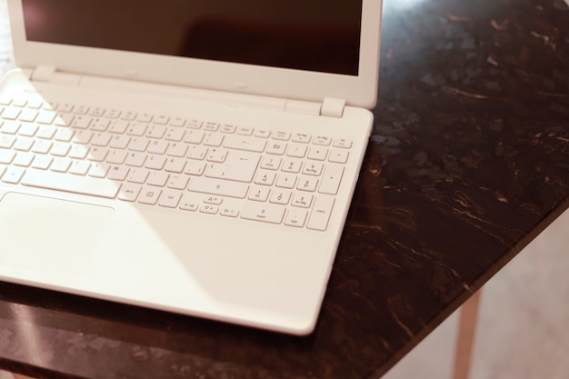 Détail d'un ordinateur portable blanc placé sur une table en marbre foncé