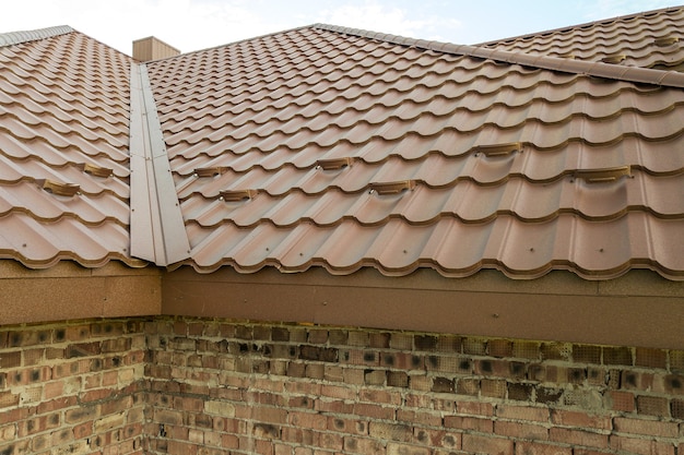 Détail de la structure du toit de la maison recouverte de feuilles de tuiles métalliques brunes.