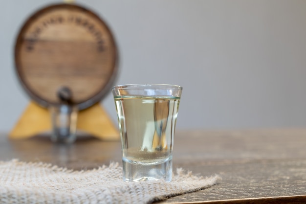 Détail de verre de cachaça blanche et cuve sur fond flou.