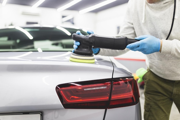 Détaillant de voiture - Travailleur avec polisseuse orbitale dans un atelier de réparation automobile. Mise au point sélective.