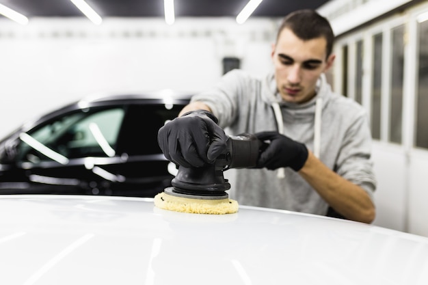 Détaillant de voiture - Travailleur avec polisseuse orbitale dans un atelier de réparation automobile. Mise au point sélective.