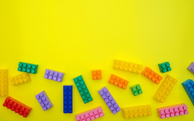 Les détails du constructeur sont dispersés sur un fond jaune. Blocs de construction multicolores.