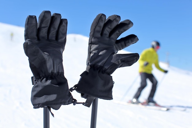 Détails sur les gants de ski noirs sur les bâtons de ski avec un skieur flou en arrière-plan par une belle journée d'hiver ensoleillée.