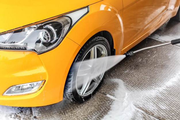 Détails sur la pulvérisation au jet d'eau du tuyau à la roue et au pneu avant de la voiture jaune, pendant le nettoyage dans le lave-auto.