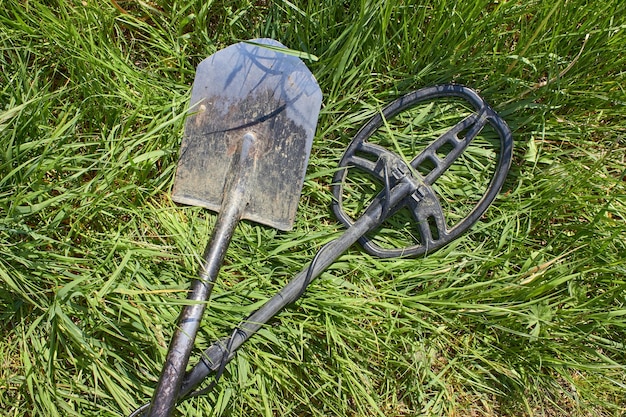 Un détecteur de métaux et une pelle pour rechercher des pièces de monnaie et des produits en métaux précieux se trouvent croisés sur l'herbe verte