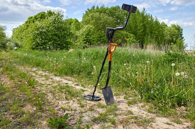 Détecteur de métaux pour la recherche de trésors et une pelle sur le fond d'une route forestière Equipement de chasse au trésor