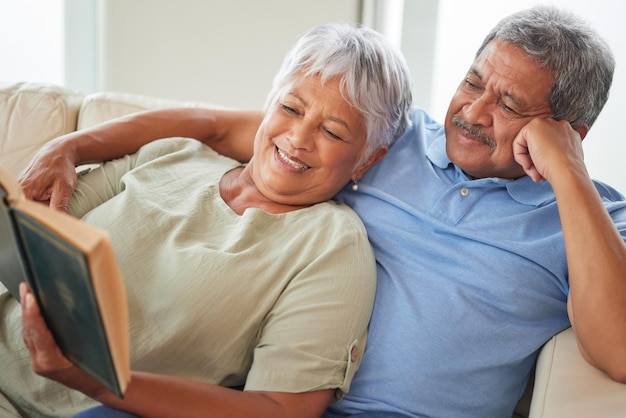 Détendez-vous un couple heureux et senior en lisant un livre ensemble à la maison tout en vous relaxant et en souriant sur un canapé Des amants matures ou âgés apprennent et se reposent tout en profitant d'une histoire comme divertissement dans la maison