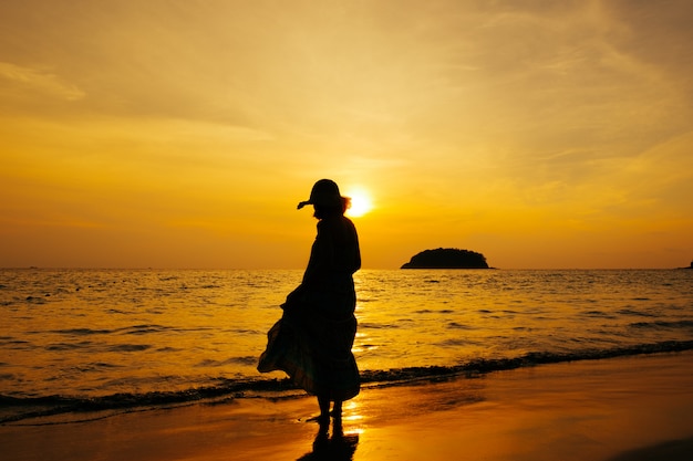 Photo détendez-vous femme debout sur la mer de la plage silhouette du coucher du soleil,