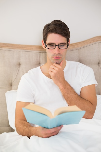 Détendu jeune homme lisant un livre au lit