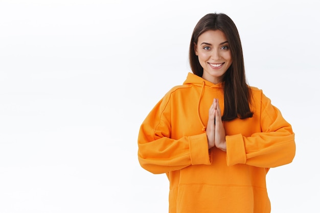 Détendue et soulagée heureuse souriante magnifique femme en sweat à capuche orange presse les mains ensemble dans prier dire namaste pratique le yoga ou la méditation soulage le stress stand fond blanc Espace de copie