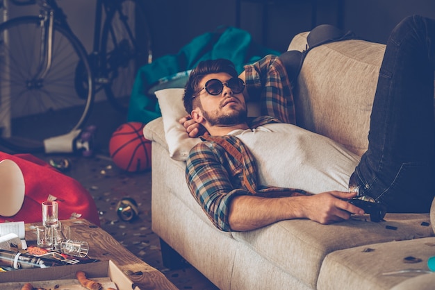 Détente après la fête. Jeune bel homme à lunettes de soleil allongé sur le canapé