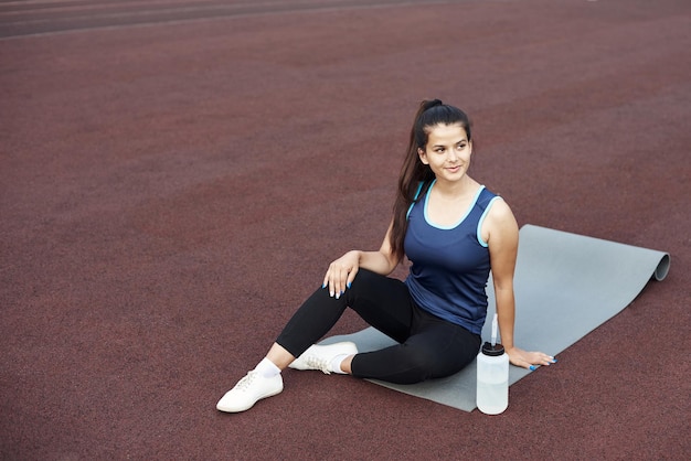 Détente après la pratique du yoga en plein air Femme se reposant sur un tapis de yoga assis dans le stade