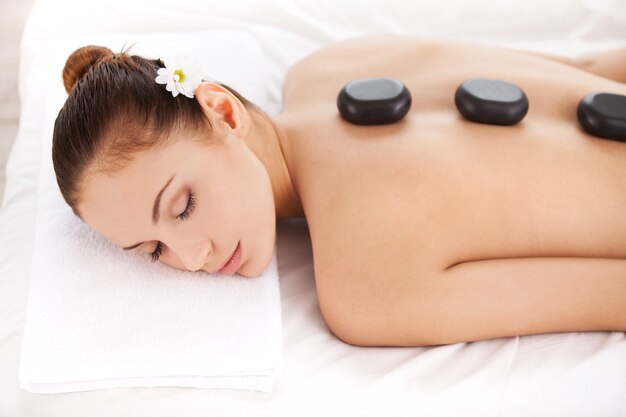 Détente au spa. Vue de dessus d'une jolie jeune femme allongée sur le devant et gardant les yeux fermés avec des pierres de spa sur le dos