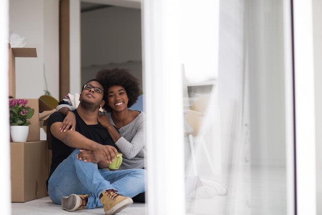 Photo détente dans une nouvelle maison. enthousiaste jeune couple afro-américain assis sur le sol et buvant du café tandis que des boîtes en carton s'étendent tout autour d'eux