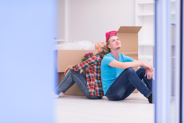 Détente dans une nouvelle maison. Enthousiaste jeune couple assis sur le sol tandis que des boîtes en carton s'étendent tout autour d'eux